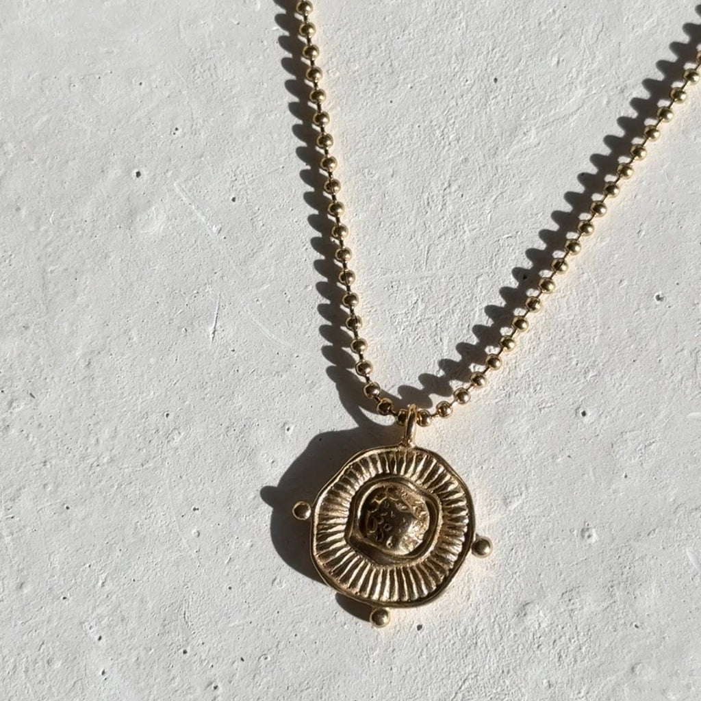 Gold necklace with a circular pendant on a light gray background