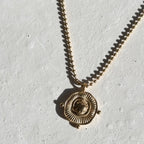 Gold necklace with a circular pendant on a light gray background